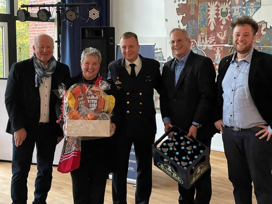 Auf dem Bild sind fünf Personen zu sehen, von denen zwei Geschenke halten. Ein Mann trägt eine Marine-Uniform.