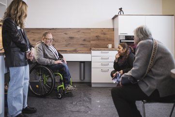 Auf dem Bild sind vier Personen in einer Küche zu sehen. Ein Mann sitzt im Rollstuhl.