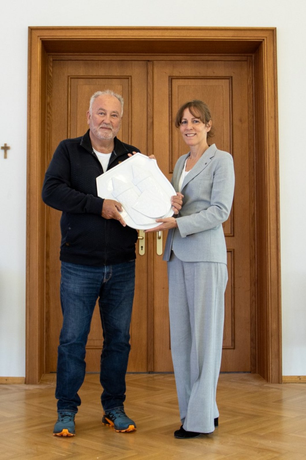 Auf dem Bild sind ein Mann und eine Frau zu sehen, die zusammen ein weißes Porzellan-Wappen hochhalten.