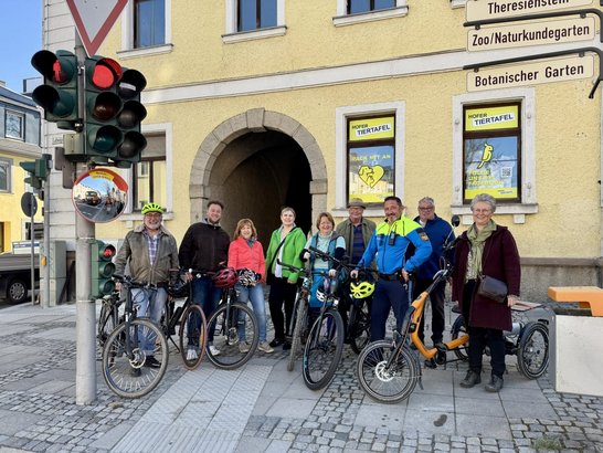 Auf dem Bild ist eine Reihe Radfahrende zu sehen, die neben einer Ampel mit Spiegel stehen.