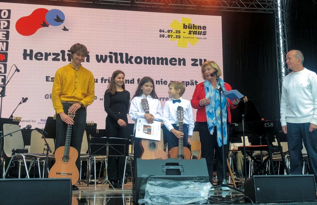 Auf dem Bild sind zwei Erwachsene zu sehen, die mit vier Kindern bzw. Jugendlichen auf einer Bühne stehen.