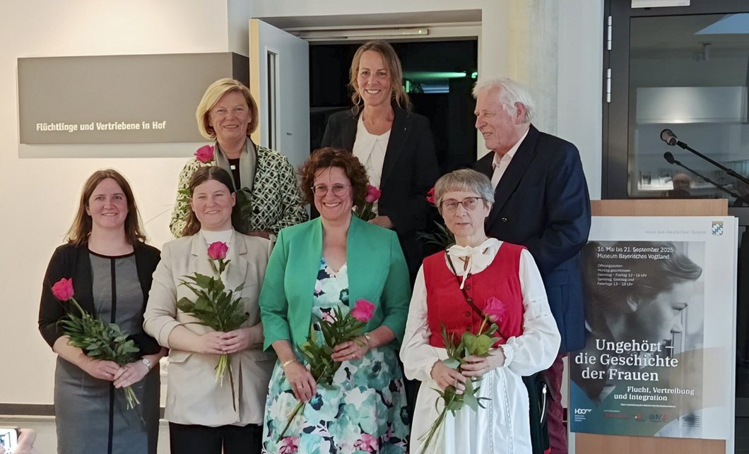 Auf dem Bild sind sechs Frauen und ein Mann zu sehen, die vor einem Rednerpult stehen und Rosen in den Händen halten.