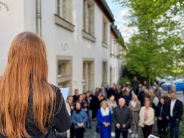 Auf dem Foto ist eine Frau von hinten zu sehen, die zu einer Menschenmenge spricht. Neben ihr steht eine Stele mit Infotext.