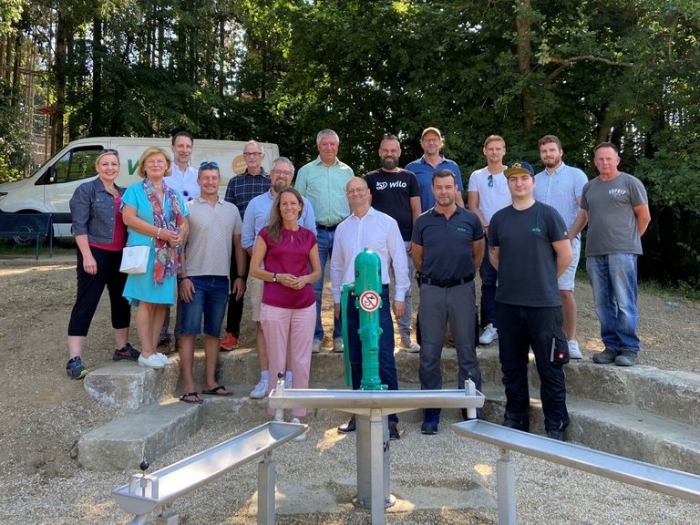 Auf dem Bild sind 16 Personen zu sehen, die hinter Wasserspielgreäten im Grünen stehen.