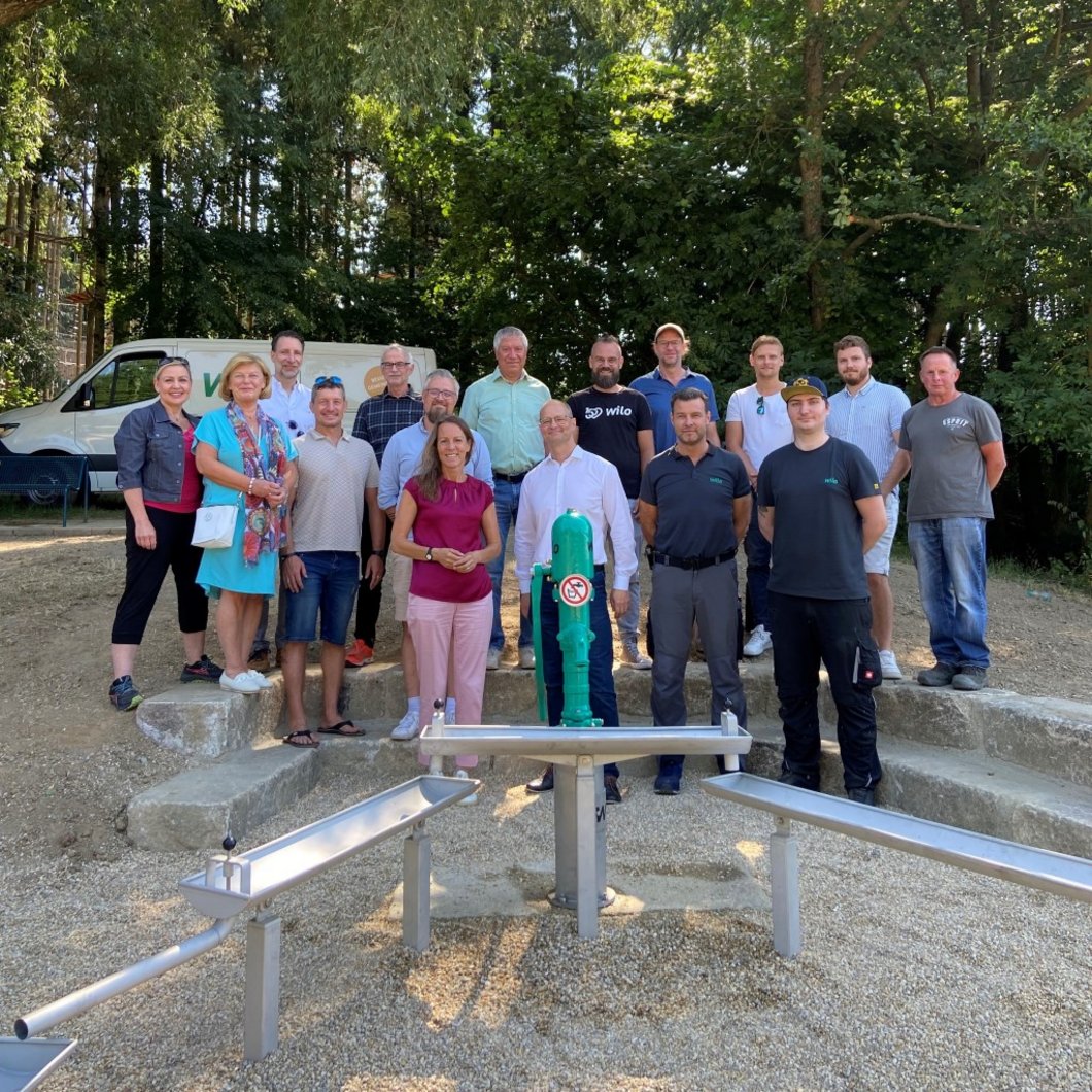 Auf dem Bild sind 16 Personen zu sehen, die hinter Wasserspielgreäten im Grünen stehen.