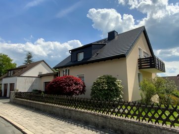 Auf dem bild ist ein zweistöckiges Einfamilienhaus mit Balkon und Garten zu sehen.