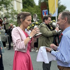 Auf dem Bild ist eine Frau zu sehen, die aus einem großen, blumenverzierten Krug trinkt.