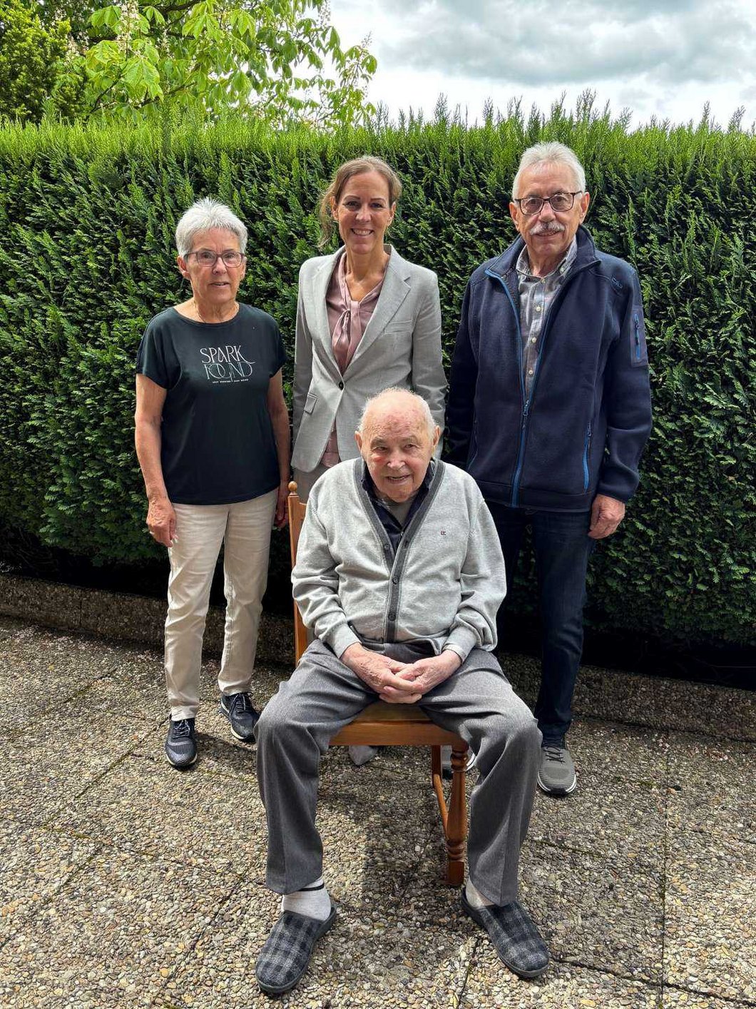 Auf dem Bild sieht man zwei Damen und zwei Herren vor einer Hecke stehen.