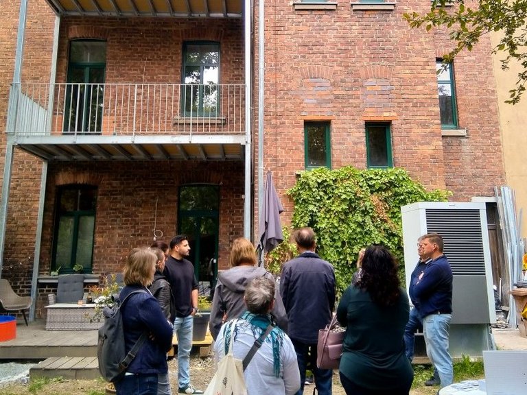 Auf dem Bild zu sehen sind Menschen, die vor einer Hausfassade stehen.