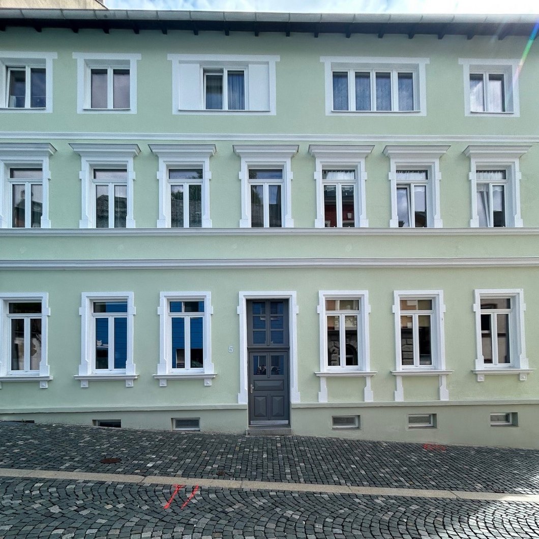 Auf dem Bild ist ein dreistöckiges Stadthaus mit grüner Fassade zu sehen.