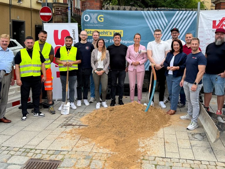 Auf dem Bild sind 16 Personen auf einer Baustelle zu sehen. Drei von ihnen tragen gelbe Westen.