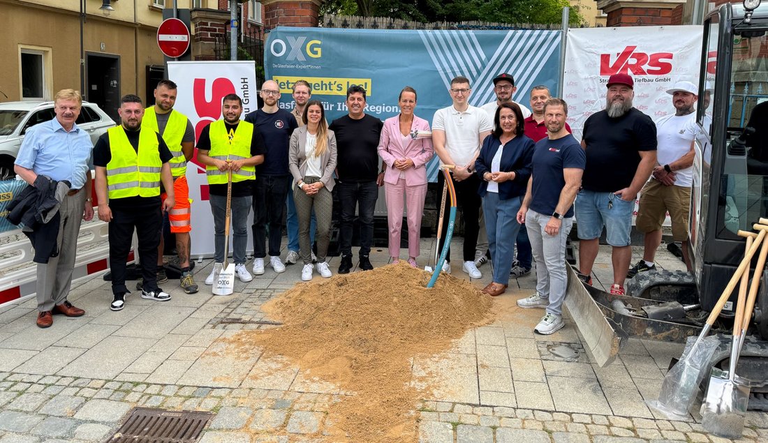 Auf dem Bild sind 16 Personen auf einer Baustelle zu sehen. Drei von ihnen tragen gelbe Westen.