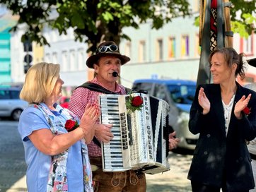 Auf dem Bild sind zwei Frauen und ein Mann zu sehen. Er spielt Akkordeon. Die Frauen klatschen.