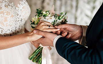 Nahaufnahme der Hände mit Blumenstrauß während der Eheschließung