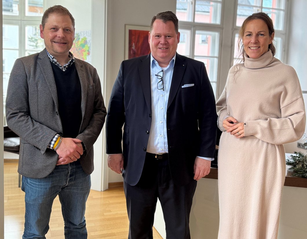 Auf dem Bild sind zwei Männer und eine Frau zu sehen, die im Amtszimmer stehen.