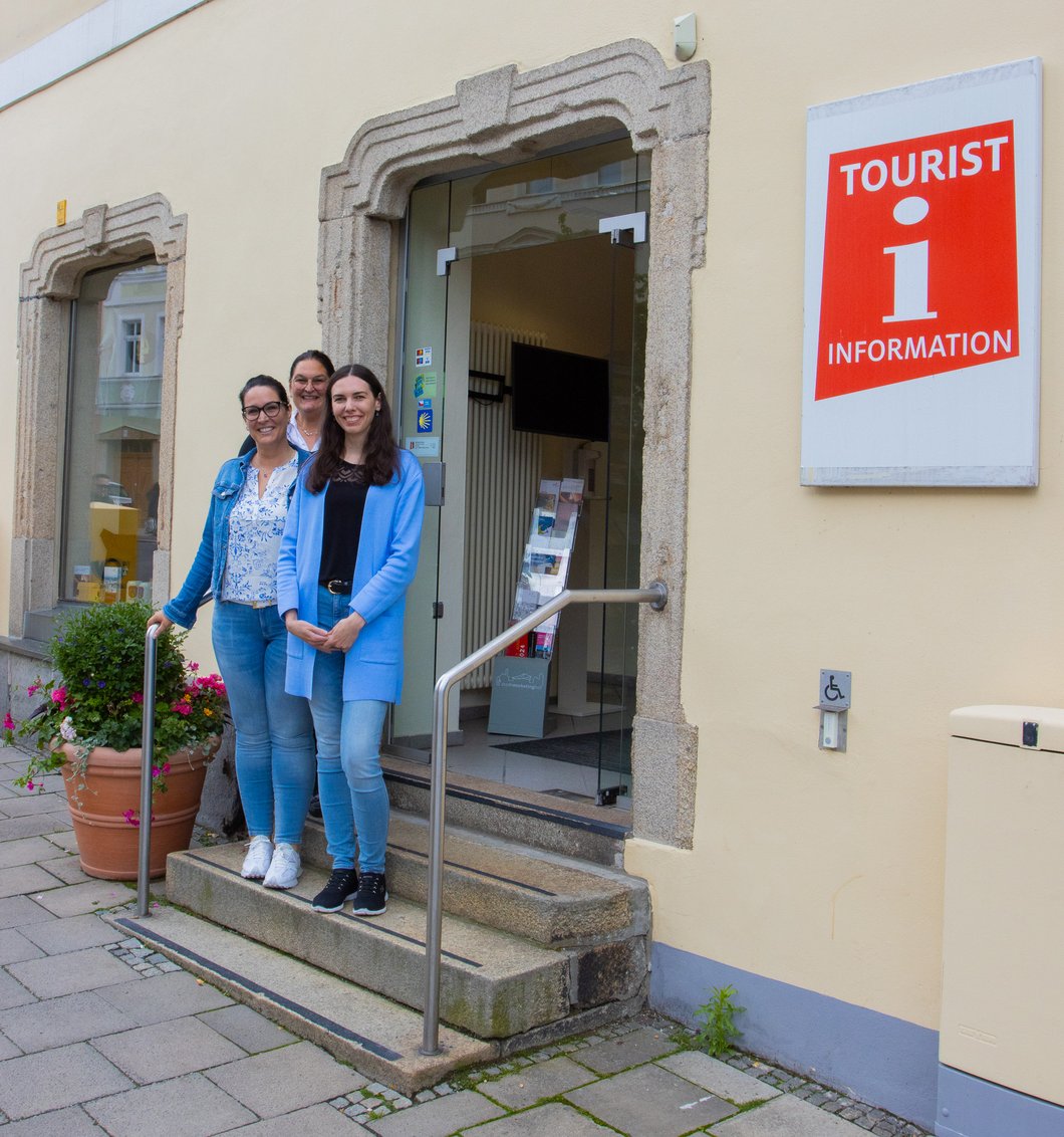 Auf dem Bild sind drei Frauen zu sehen, die nebeneinander stehen und lächeln.