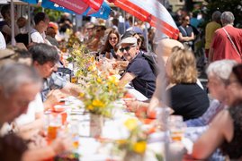 Auf dem Bild sind Menschen an einer langen, mit Blumen geschmückten Tafel zu sehen.