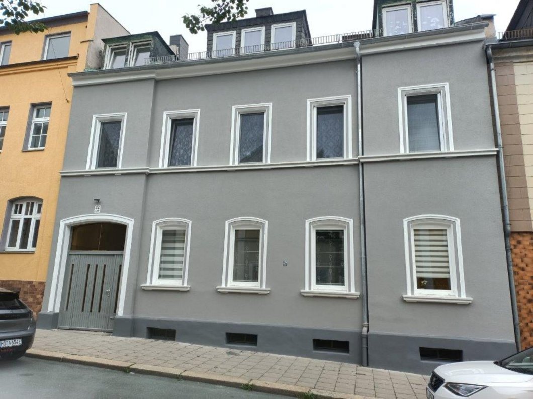 Auf dem Bild ist ein dreistöckiges Stadthaus mit dunkelgrauer Fassade zu sehen.