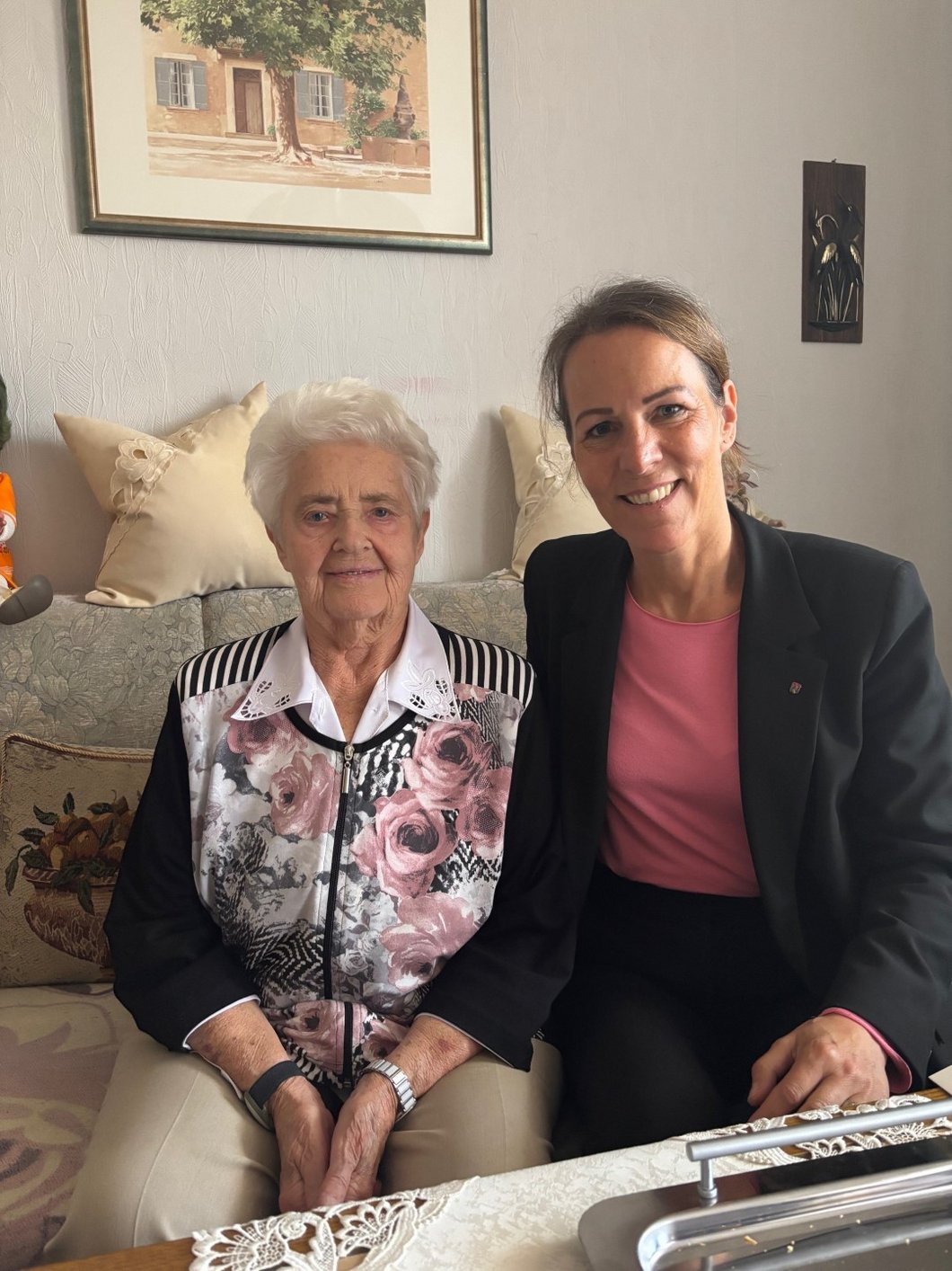 Auf dem Bild sind eine alte und eine jüngere Frau zu sehen, die auf einem Wohnzimmersofa sitzen.