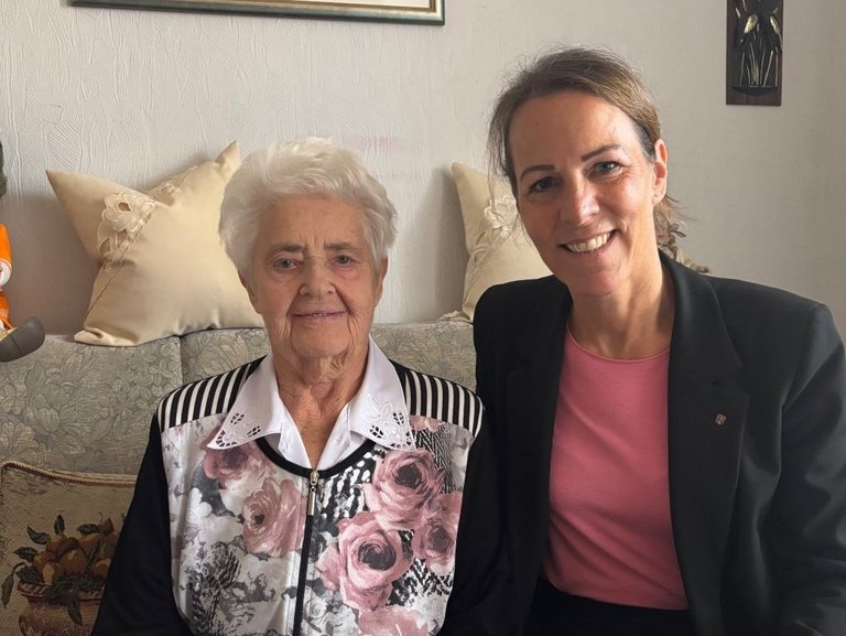 Auf dem Bild sind eine alte und eine jüngere Frau zu sehen, die auf einem Wohnzimmersofa sitzen.