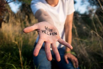 Auf dem Bild ist die geöffnete Hand einer Person zu sehen, auf der "Wir helfen" steht.