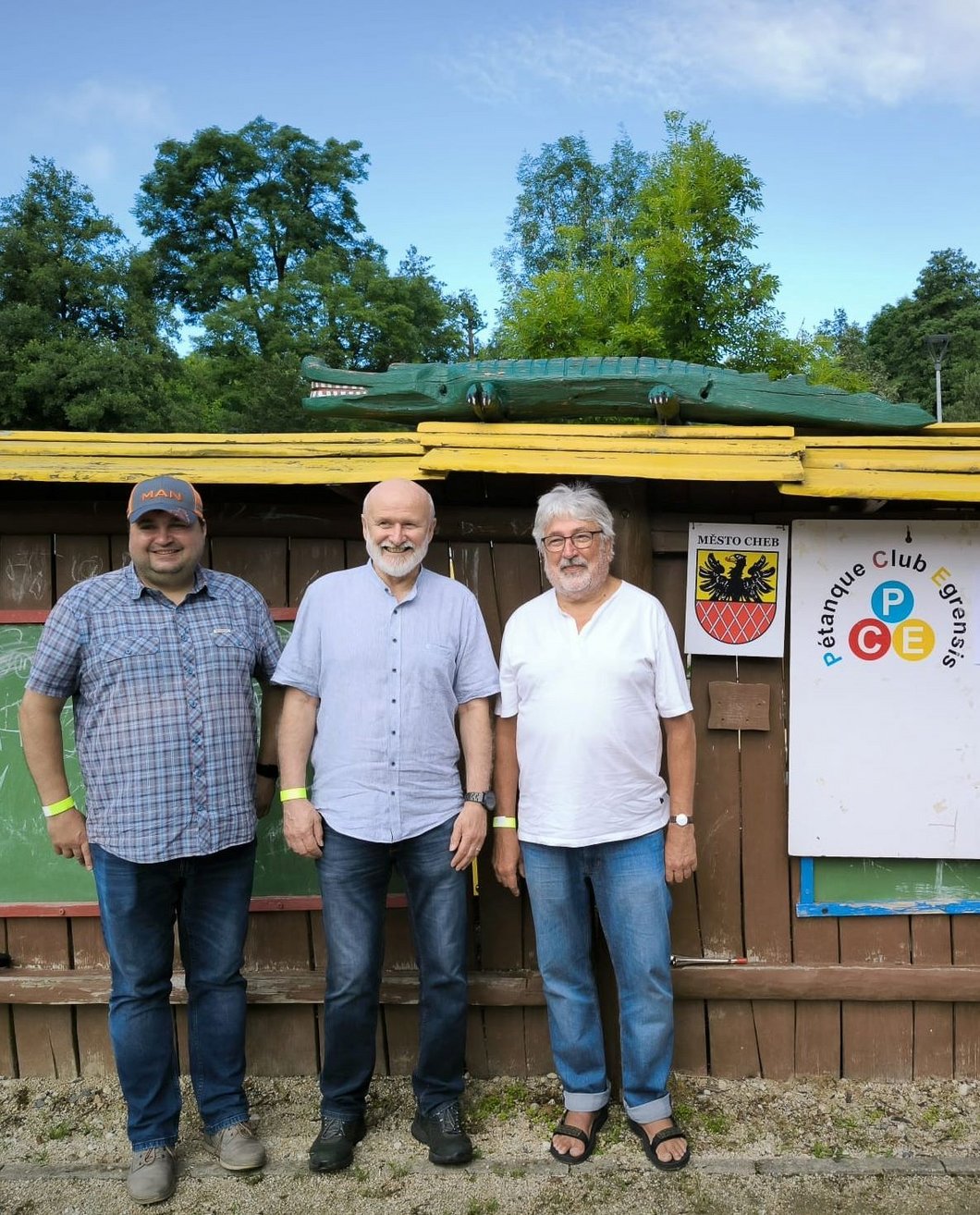 Auf dem Bild sind drei Männer zu sehen, neben ihnen das Wappen der Stadt Cheb und das Logo des Petanque Club Egrensis.